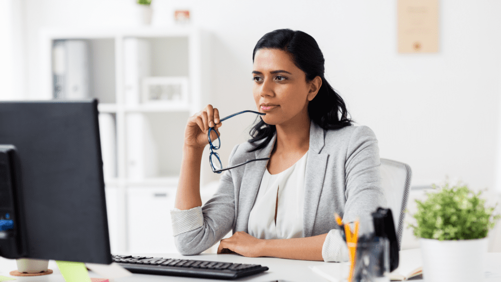 A paralegal sitting at her desk with her glasses and thinking deeply, showing one of the habits of the indispensable paralegal.