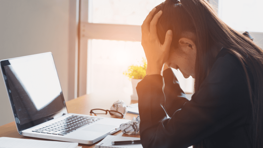 Frustrated paralegal sitting at a desk holding head in hands due to attorney work style mismatch.