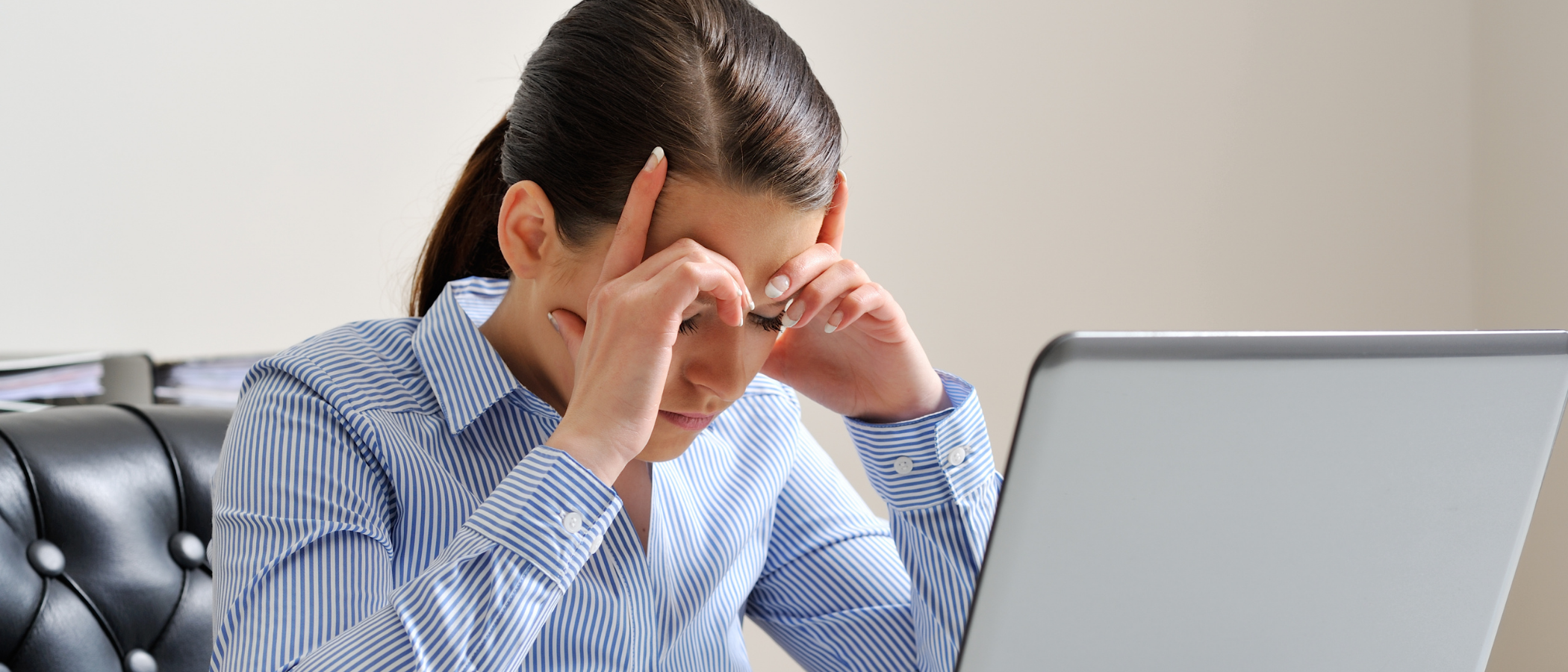 Stressed female paralegal rubbing her temples at a desk with a laptop, dealing with new paralegal anxiety and workload ambiguity.