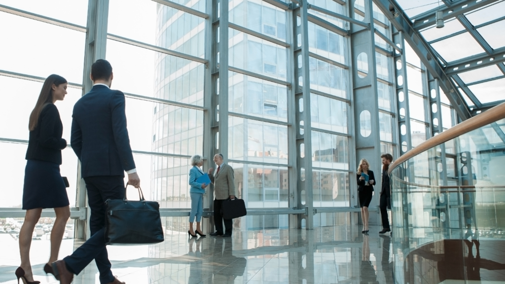 Two attorneys standing close to a firm's glass wall and discussing the necessity of billable hour bootcamp for law firms.
