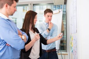 A female co-worker placing sticky notes on the wall as two other coworkers try to figure out a solution