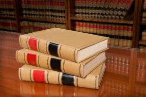 A stack of three law books on a table with many others on the shelf in the background