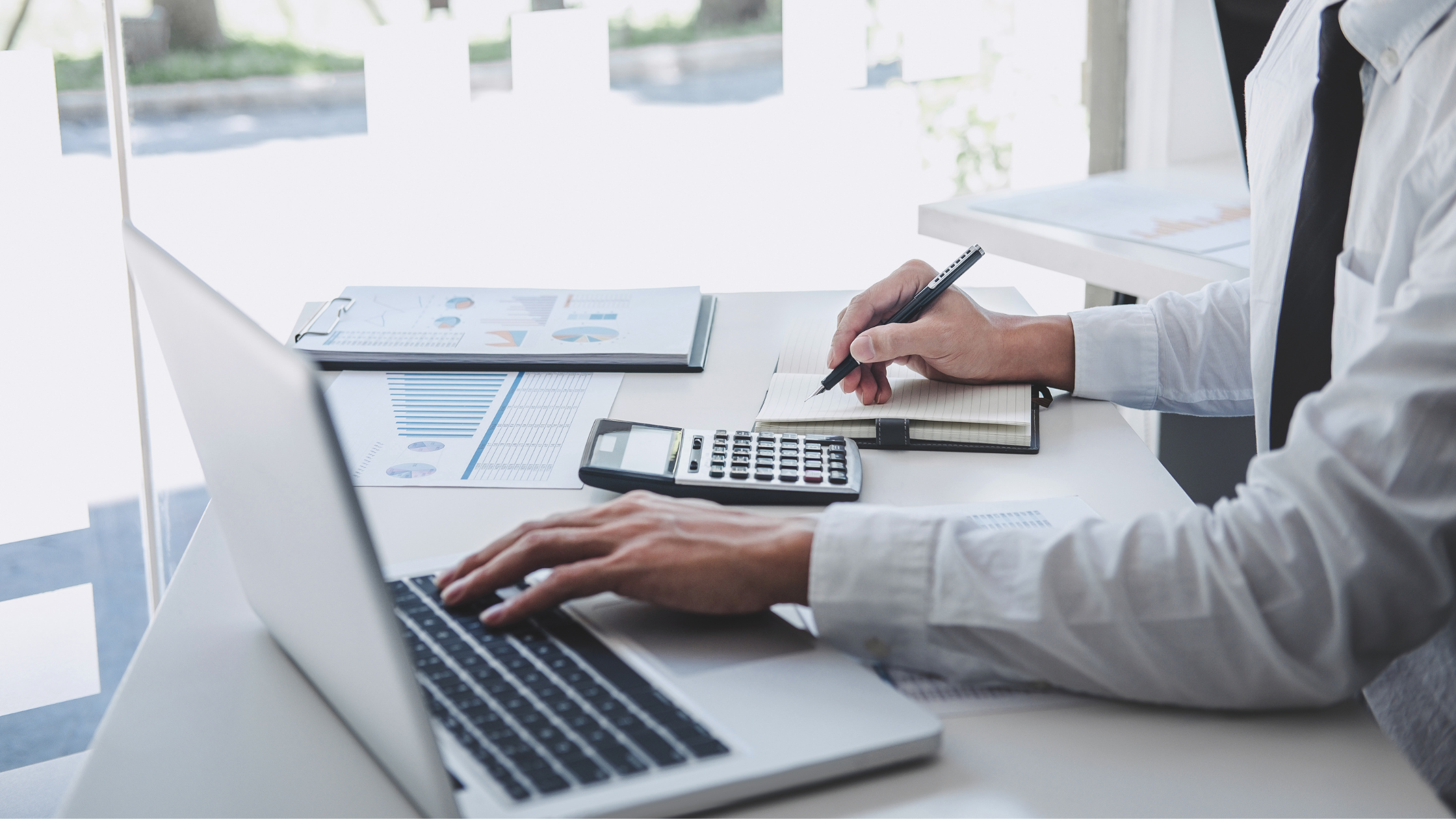 A paralegal drafting billable time entries with a laptop, a pen, a notepad, and a calculator.