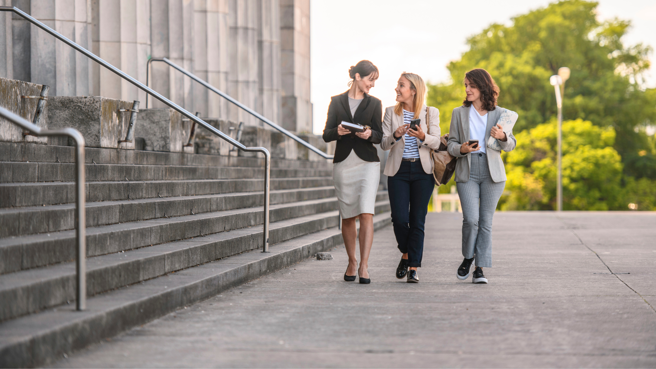 Three paralegals walking with their course materials as they navigate the path from paralegal to lawyer.