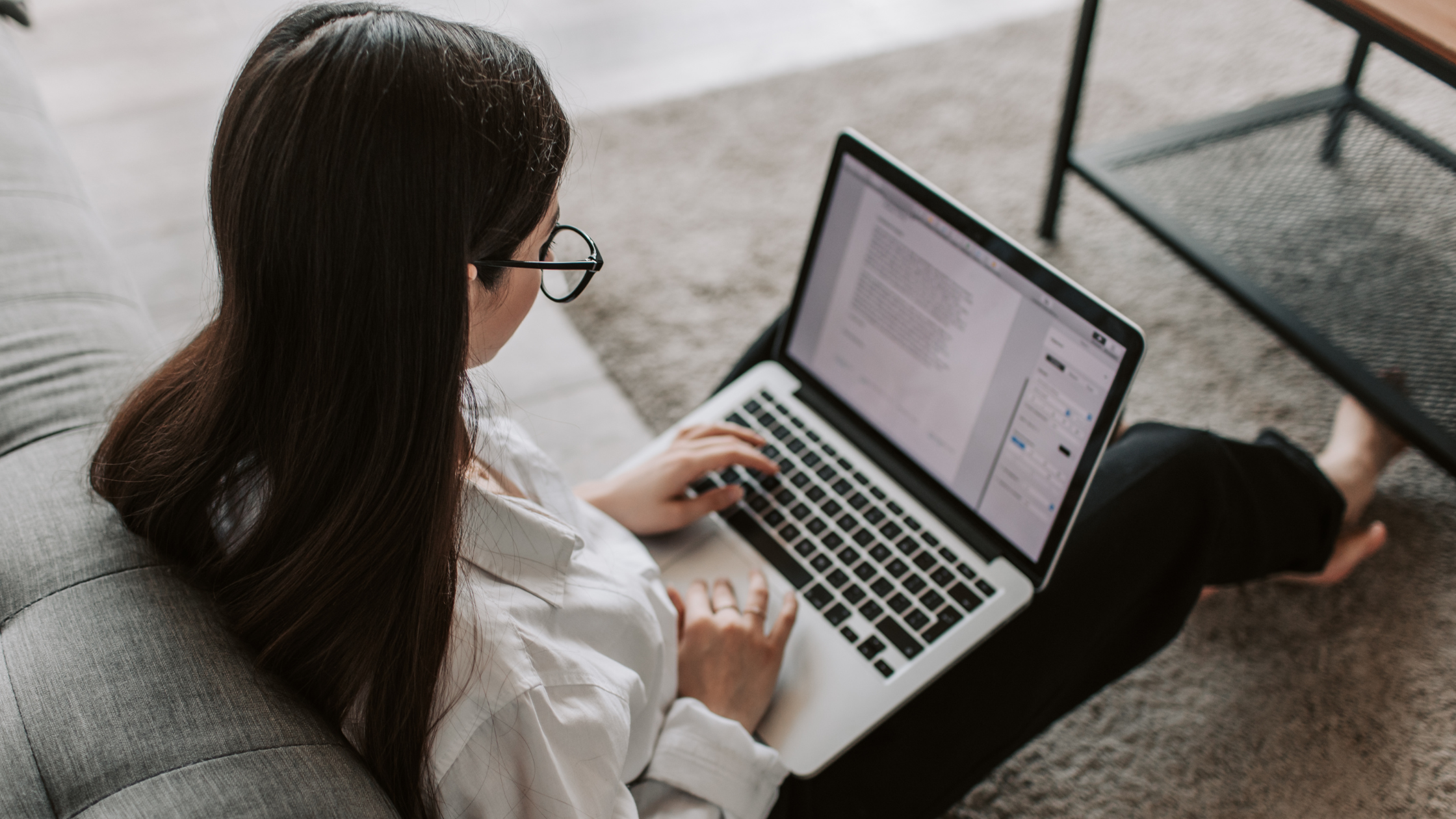 A freelance paralegal sits on the floor in her apartment with her computer on her lap and continues to work.