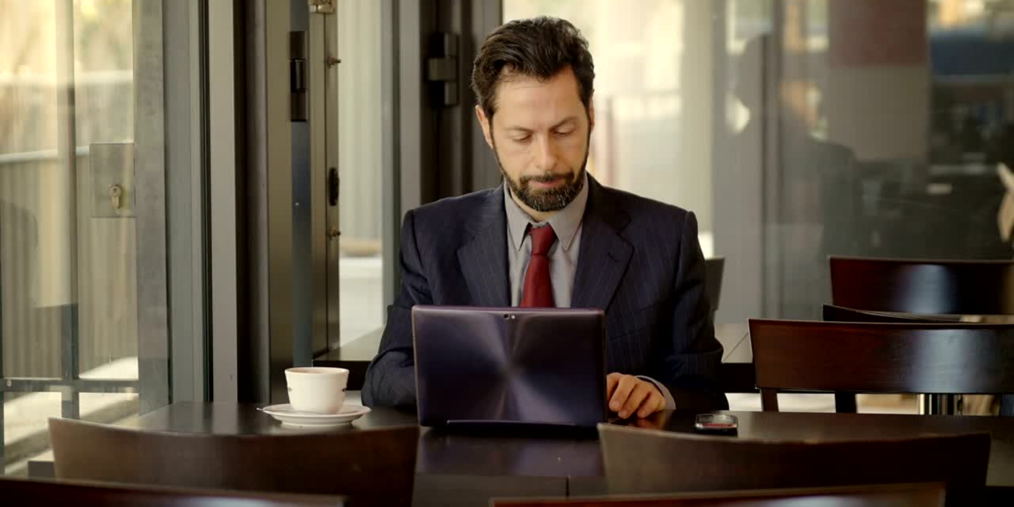 A paralegal in his office working with a tablet and a cup of coffee on the table.