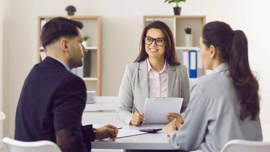 A paralegal holds papers and a pen and sits with two clients as they discuss their case.