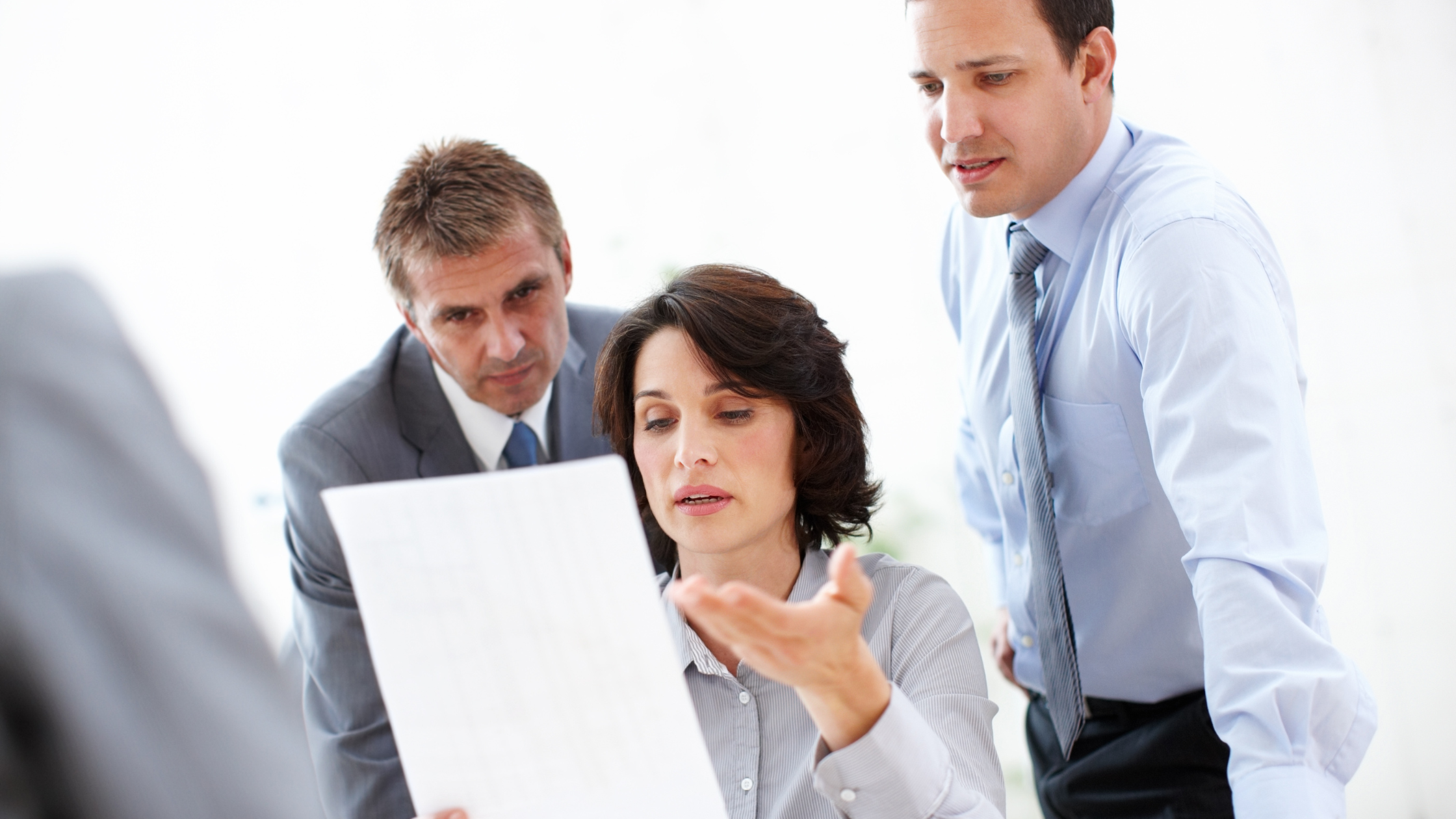 Two paralegals stare at a paper a third paralegal is holding while the third paralegal is relaxed and giving a solution.