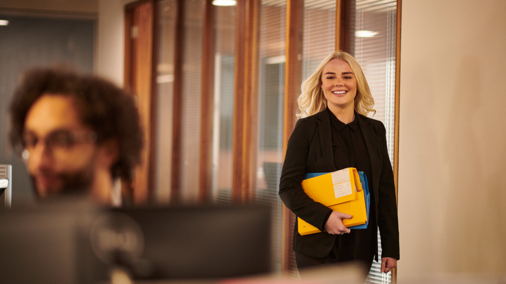 A relaxed paralegal strolling into an office with an official envelope while a broad smile sets in her face.