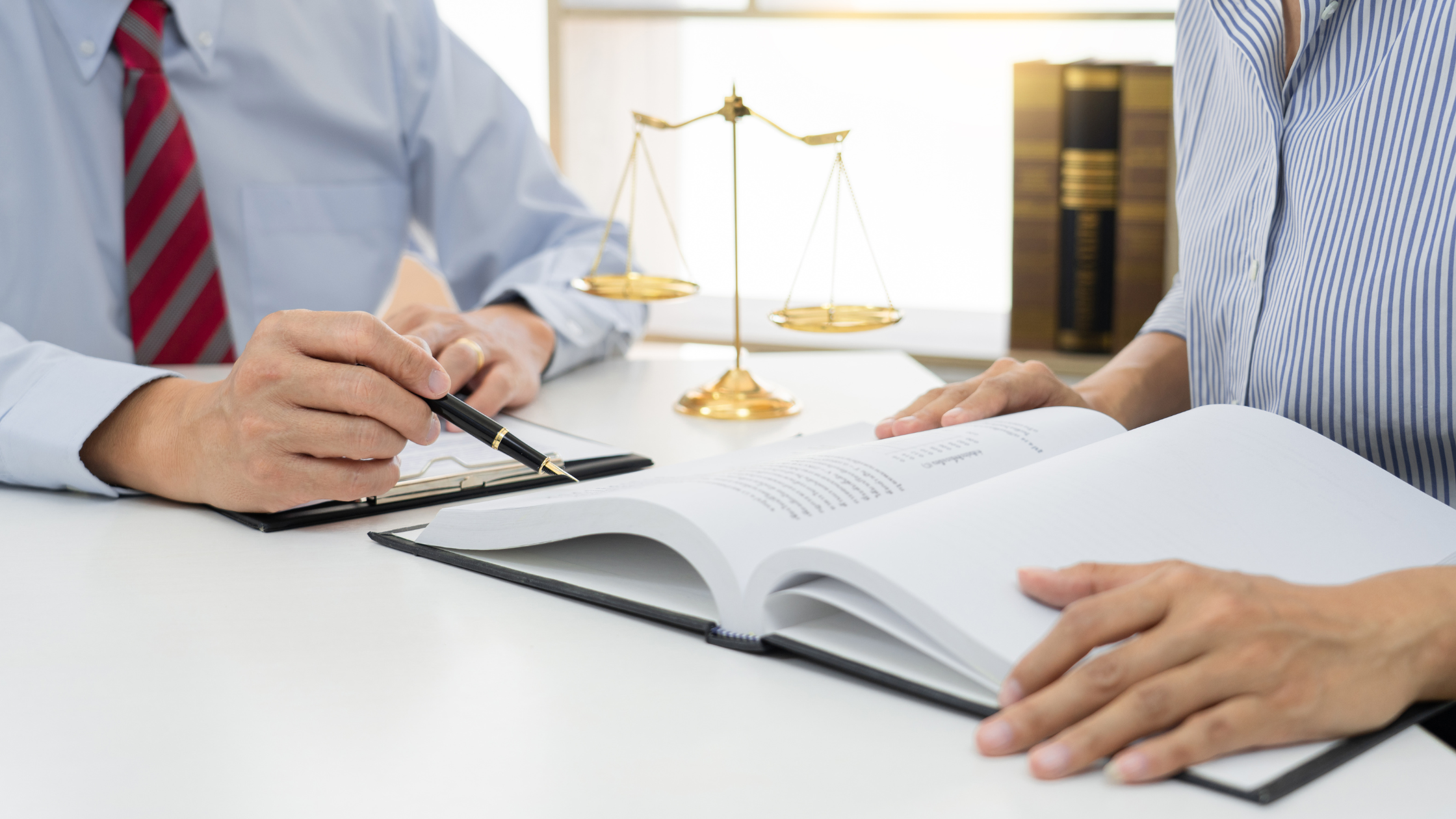Two paralegals sit at a desk with a justice scale and a boom studying what a public defense paralegal is.