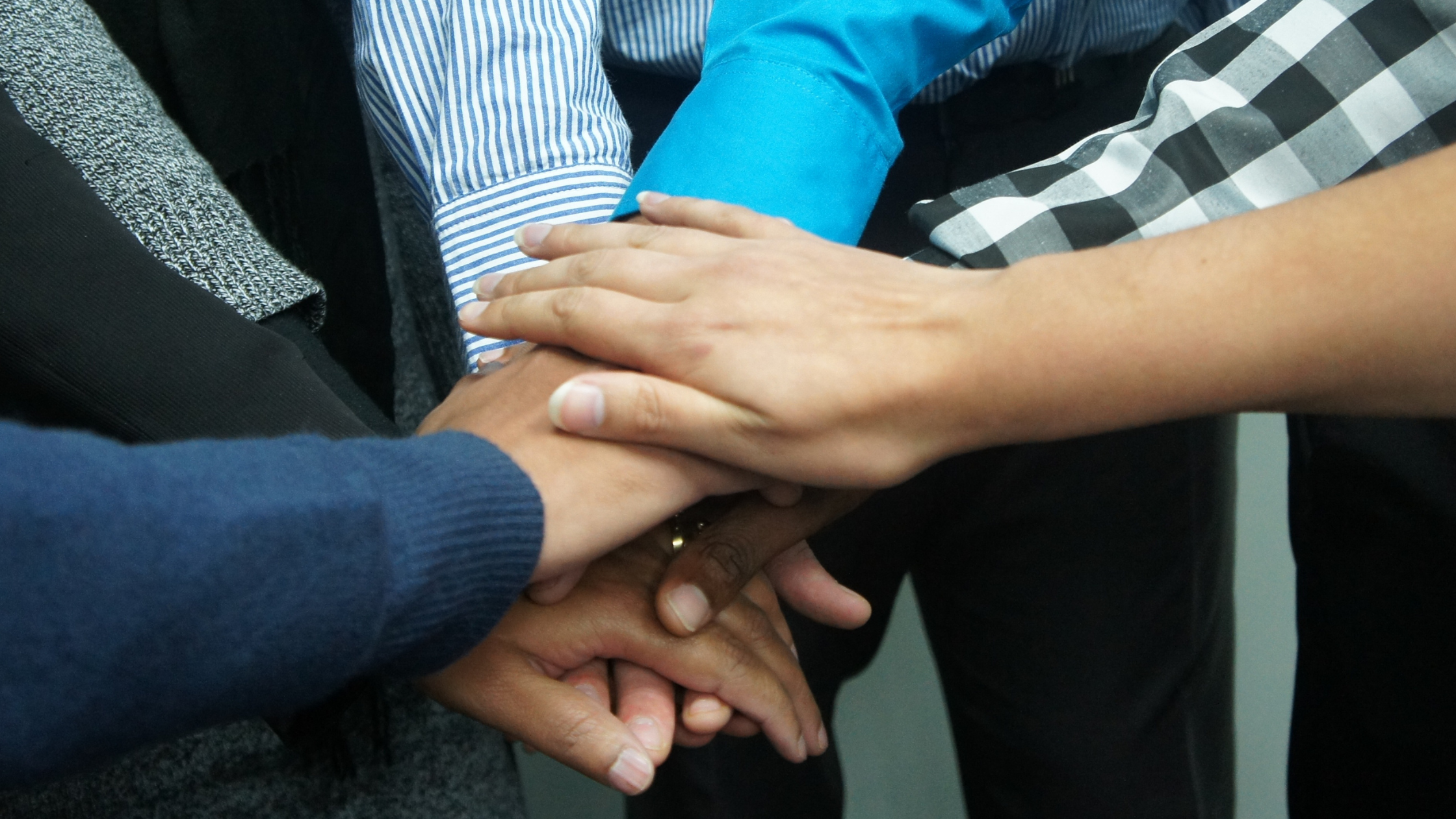 A group of paralegals stack their hands on one another in a show of support against the scarcity mindset among paralegals.