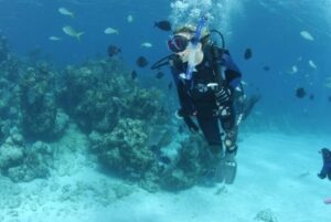 A scuba diver with an oxygen tank and mask at the bottom of the sea with different fishes swimming around