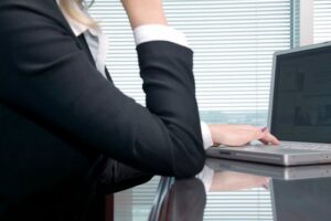 A woman at her desk working on a paralegal project on her computer with her left hand on the keyboard