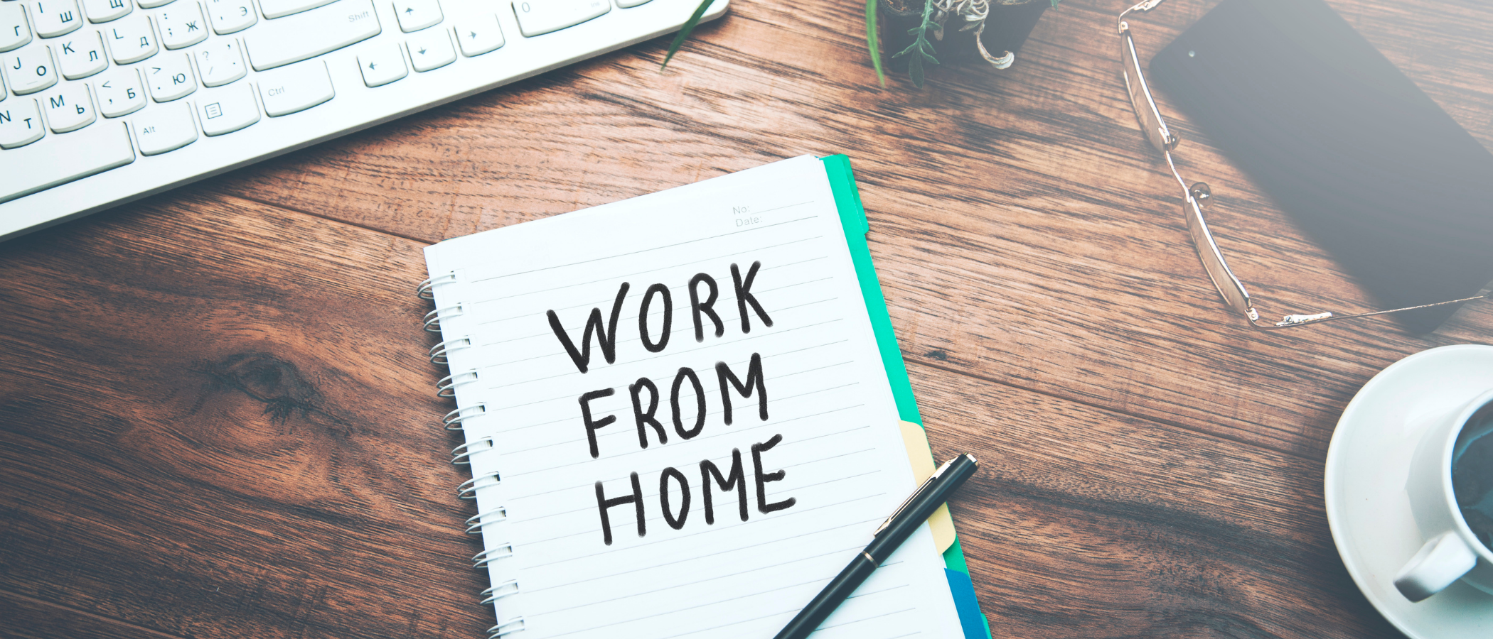 A note illustrating the words “work from home” on a notepad on a wooden desk